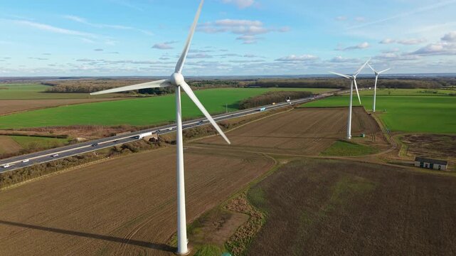 Cinematic panning aerial drone view of wind turbines near the M1 motorway in England during golden hour highlighting UK renewable energy infrastructure.