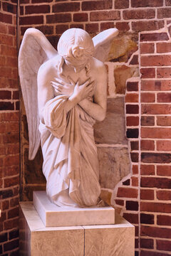 Helsingborg, Sweden - 12 August 2025: View of a pale angel statue kneeling in solemn reverence against the rich, dark brickwork, a study in light and shadow.