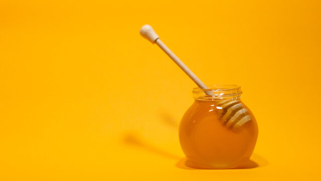Honey dipper in a glass jar of honey on a yellow background. Minimal food concept with copy space.