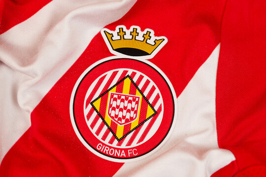 Close-up of the Girona FC football club crest logo on a red and white striped official team jersey fabric.