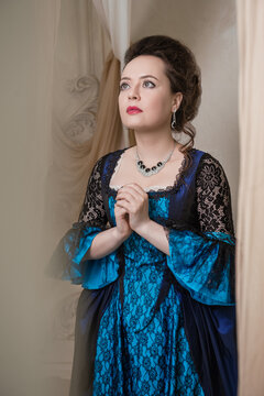 Beautiful woman wearing blue medieval dress praying stands among ancient ruin
