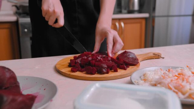 Sliced boiled beets are folded and diced on a platter, the home cook lays out the red cubes for the salad bowl, the visible grated carrots and plates on the countertop, neatly sliced and served neatly