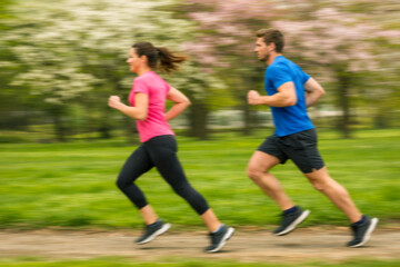 Young fitness couple in sportswear running together in park with action motion blur. Healthy lifestyle and training concept.