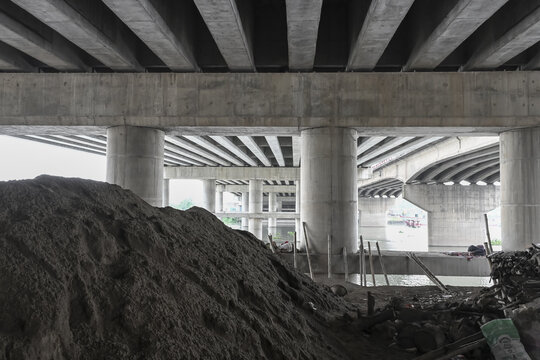 Dhaka, Bangladesh - 11 September 2025: View of the stark concrete underbelly of the flyover contrasts with the rough texture of the sand pile below.
