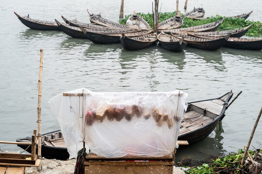 Dhaka, Bangladesh - 09 September 2025: View of fishing boats resting on the water's edge, a street vendor stall covered in plastic, and the muddy riverbank.