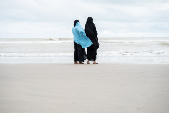 Cox's Bazar, Bangladesh - 08 August 2025: View of two women standing on the sandy beach, one draped in a vibrant blue shawl, against the backdrop of the muted, grey ocean and sky.