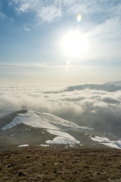 Valley clouds cover Angren city in Winter with power transmission towers visible on a hill above clouds.