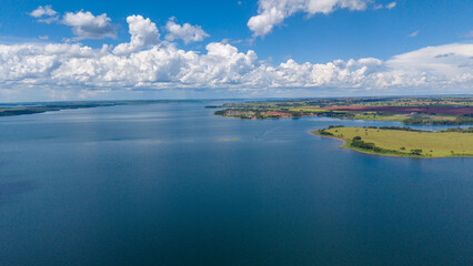 Fototapeta premium A serene aerial view of a vast body of water surrounded by lush green land and a vibrant blue sky
