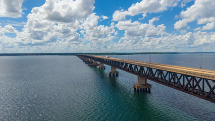 A long bridge stretches across a large body of water under a blue sky with fluffy white clouds