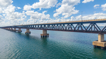 A large steel bridge spans across a body of water under a blue sky with white clouds