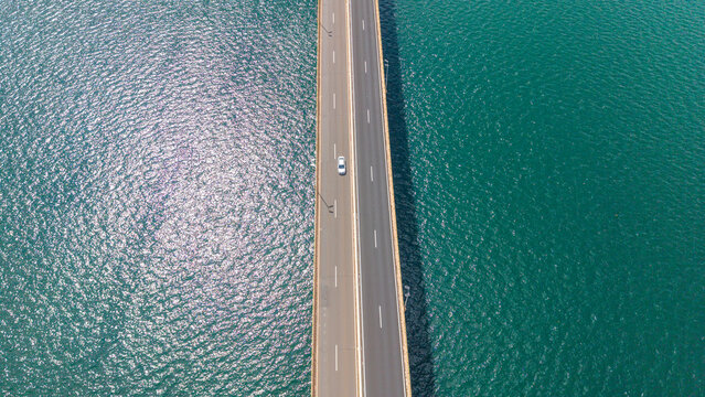 Aerial view of a long road bridge over a large body of water with a car driving on it