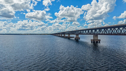 Fototapeta premium A long bridge stretches across a large body of water under a blue sky with fluffy white clouds