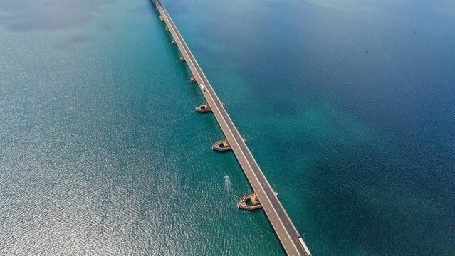 An aerial view of a long bridge stretching across a vast body of water with varying shades of blue