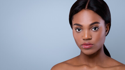 A woman with long dark hair stands in front of a light blue background. She looks directly at the camera with a neutral expression. The lighting highlights her features and skin tone. © Prostock-studio