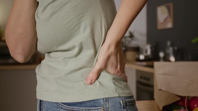 Close-up of face and midsection of young Caucasian woman rubbing neck and back, stretching lumbar spine, after experiencing painful muscle spasm, suffering from arthritis or hernia, alone at home