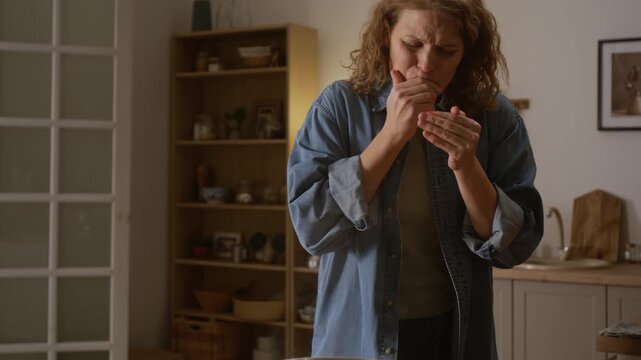 Medium shot of mature Caucasian woman cooking lunch in kitchen, grabbing steaming hot cooking pot with soup from stove, burning hands, grimacing, crying in pain, shaking fingers and putting in mouth