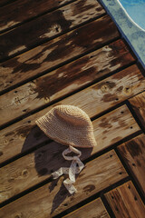 The girl's straw hat lies on the wooden floor near the pool. Fashionable hat with lace ribbons of a little girl. Relaxation at the pool. Vertical photo. Free space for logo, text.