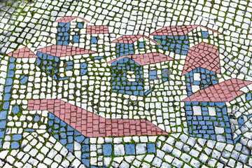 Obraz premium High-angle close-up of a traditional stone mosaic pavement depicting stylized houses with pink roofs and blue walls,