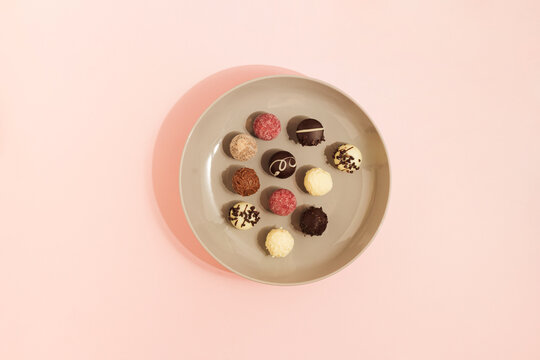 Chokolate candies in various colors on a gray retro plate. Sweet arrangement on pink background. Flat lay.