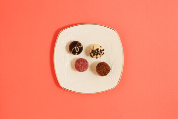 Chocolate candies in red, cream and brown colors on a white plate. Sweet concept on pink background, flat lay. © Suzana