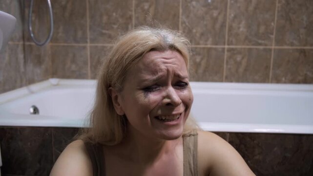 Violence against women, mental disorder, loneliness and fear concept. Blonde woman crying in bathtub, mascara stains, streaming tears, sorrowful gaze, tiled bathroom background, despair, depression