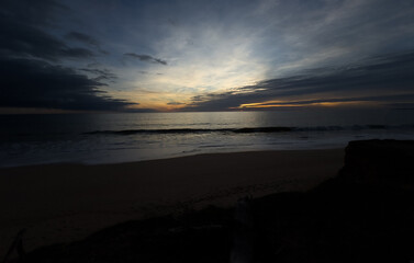 Beautiful sandy beach with red rocks and cliffs. Sunset at dusk with shallow waves on the Atlantic coast in Praia de Loule Velho, Algarve, Portugal
