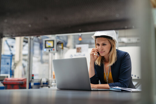 Female factory supervisor talking on phone in industrial production hall.
