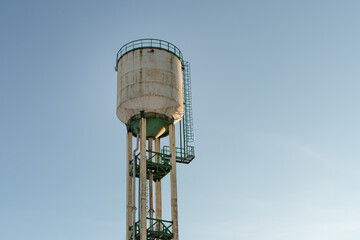 A water tower illuminated by the rays of the evening sun. A tall water tower against a blue sky.