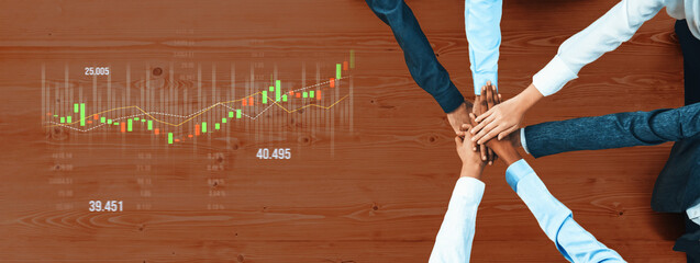 A diverse team collaborates in a professional environment, joining hands over financial data,...