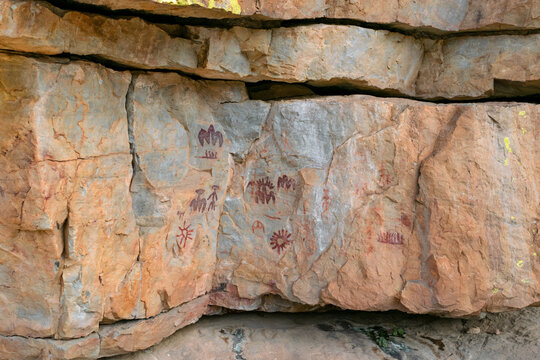 Schematic anthropomorphic and solar motifs painted in red on limestone in La Batanera, Fuencaliente, Spain.