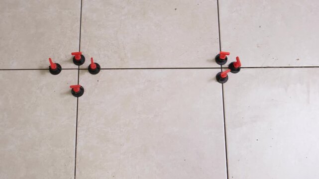 Worker Laying Ceramic Tiles on the Floor. Repairman Placing White Gray Square Tiles, Applying Adhesive. Builder Installing Tile Using Leveler, Tile Leveling Clips. Tiling. Finishing Repair Work. 4K