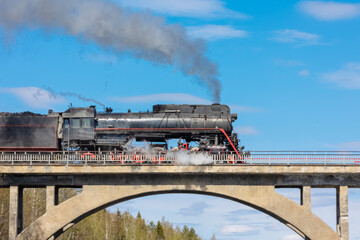 A retro steam locomotive travels across an old railway bridge. © Sergey