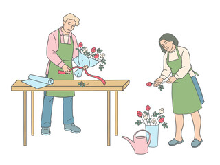 Male florist tying ribbon around bouquet at table and female florist holding rose