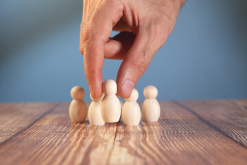 Businessman's hand arranging wooden figures of people on a wooden table.