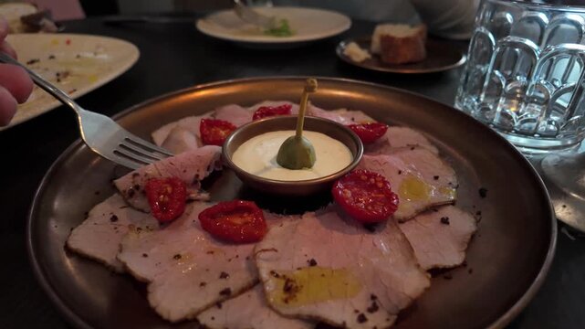 Customer eating a traditional italian appetizer, vitello tonnato, composed of thinly sliced veal with a creamy tuna and caper sauce and tomatoes, served as a gourmet starter in a restaurant