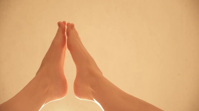 Close-up of a woman's bare feet touching each other, with a warm, soft light. Zen-like pose. Clap your feet. Creative applause. Beige background. White soft skin. High quality 4k footage.