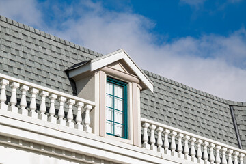 A gray roof with dormer window against a bright blue sky with white clouds