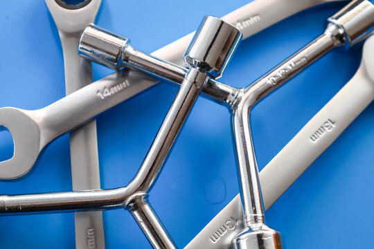 Professional combination wrenches and lug tools lie on a vibrant blue background. High-quality steel equipment with clear size markings is designed for precise automotive maintenance and complex repai