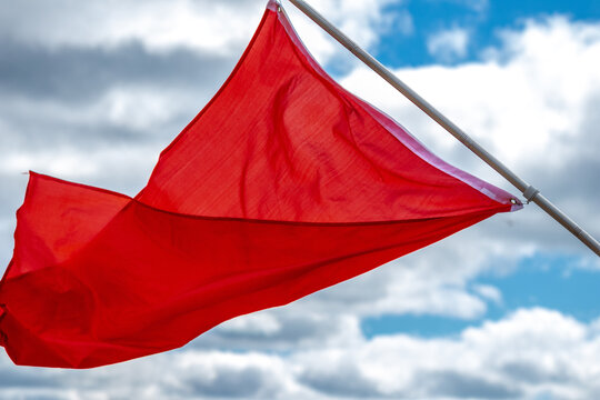 Red warning flag flying in the wind against blue sky, close up.