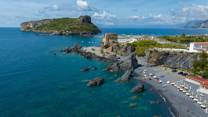 Aerial view of Fiuzzi Beach, located in the province of Cosenza, Calabria, Italy. There is a low coastal watchtower overlooking the sea and the island of Dino in the background. It's a sunny morning.