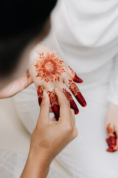 Groom Placing Diamond Ring on Bride's Hennaed Hand.A close-up shot of a grooms hand sliding a diamond ring onto the finger of a bride decorated with intricate red henna patterns.