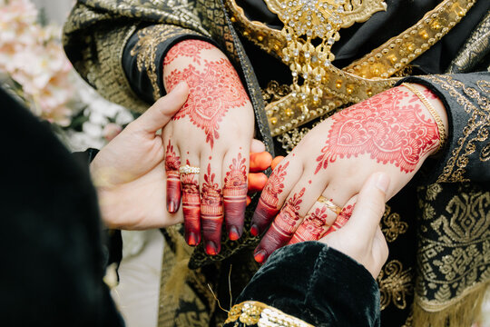 Couple Holding Hands Showcasing Wedding Rings and Henna.A top-down view of the bride and groom's hands joined together, highlighting the matching wedding bands and the bride's intricate henna art.