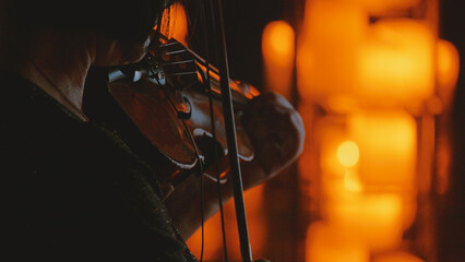 Close-up of a violinist performing in a dark, intimate setting. The musician is silhouetted, lit by...