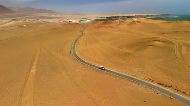 Aerial drone view of a car driving in Paracas. The Pacific Ocean and cliffs of Paracas. Dramatic Pacific landscape. Panoramic coastal view. Peru, Ica Region.