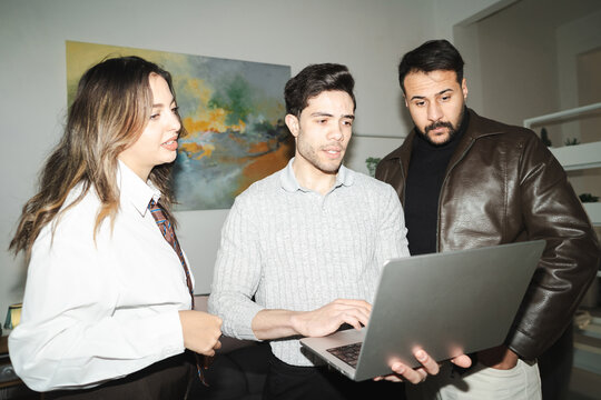Three colleagues collaborate on a project, gathered around a laptop. They are engaged in discussion and problem-solving, working together to achieve a common goal.