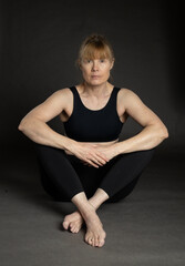 Fit mature woman in her fifties sitting on floor in studio wearing workout clothing