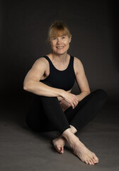 Smiling older woman wearing fitness attire sitting on floor in studio
