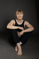 Active woman in her fifties with strong arms sitting on floor in studio wearing workout clothing