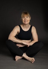 Older woman wearing workout clothing sitting on floor in studio showing fit body