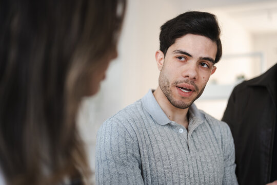 A young man in a grey polo shirt speaks animatedly to another person, engaged in a conversation.